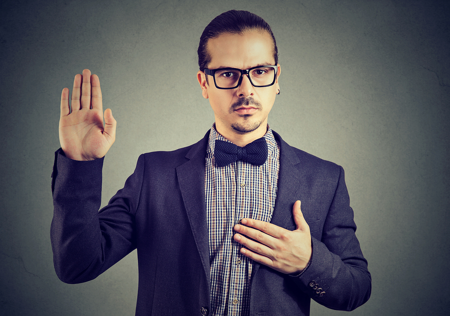 Young man in formal clothing and eyeglasses swearing in being trustworthy while looking at camera.