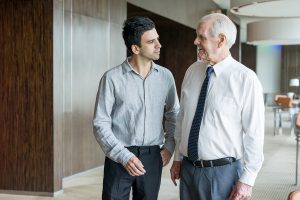 Two office employee walking along office space. Junior employee listening to senior mentor in white shirt and tie. Business meeting and coaching concept
