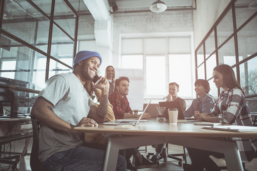 Pleasant call. Low angle of friendly young positive team is sitting around table in office and discussing business project. Caring leaders create engaged culture.