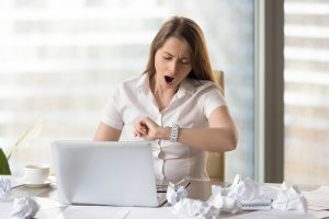 Young businesswoman yawning while working on laptop in office. Sleepy female entrepreneur looking on wristwatch. Tired office worker feels lack of sleep because of hard and long work with documents